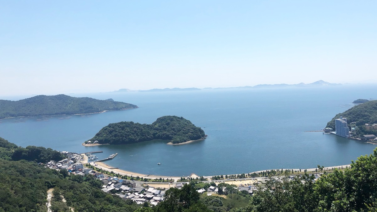 山の上から見下ろした坂越湾。湾の中ほどに緑の島が浮かび、手前に港町が見える