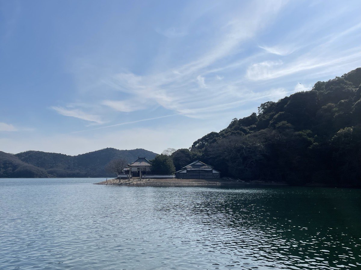水辺に鳥居と社殿が建ち、後ろに緑の山が連なる風景
